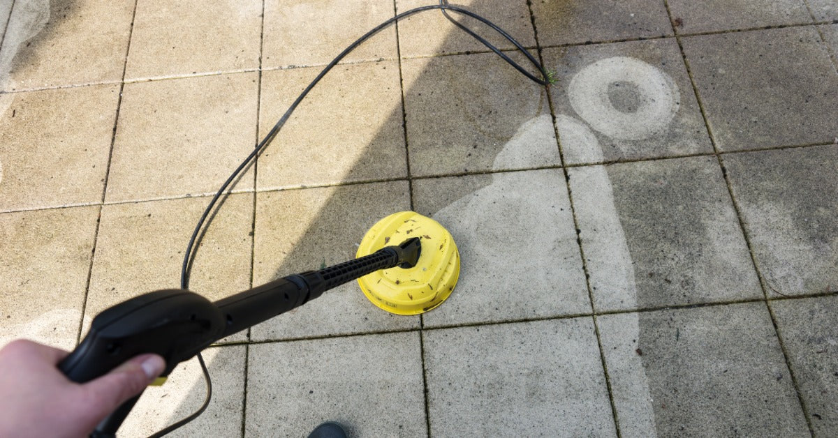 a pressure washer with a yellow surface cleaner moving across square patio tiles with wet and dirty sections.