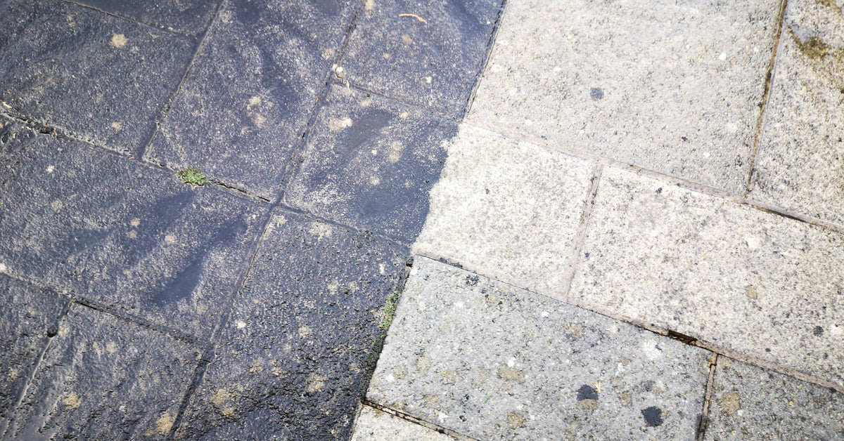 A close-up of a stone patio with two sides: one clean and one dirty. The dirty side looks black with dirt and growth.