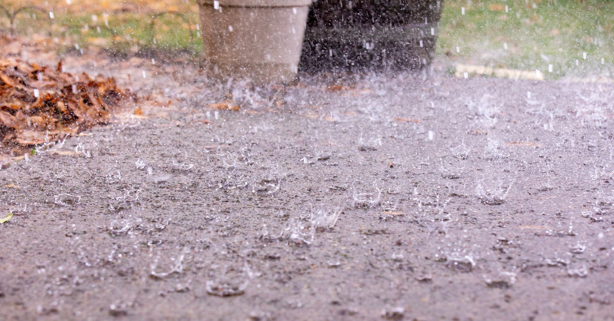 A dark-colored patio completely covered by a layer of water and dead leaves as a harsh rain falls down on the surface.