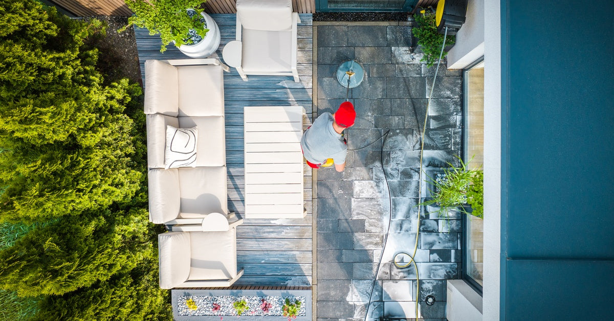 A top-down view of a person wearing a red hat operating a patio cleaning machine, washing the stones.