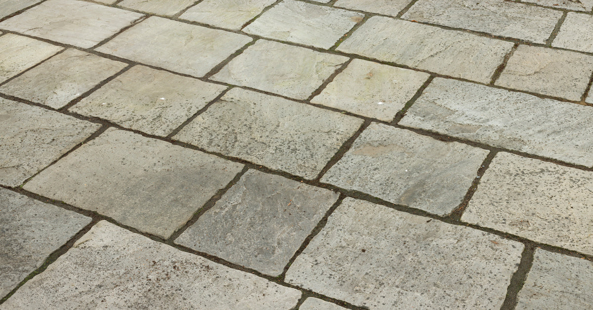 A close-up of a stone patio with black spots and moss growing between the cracks of each stone.